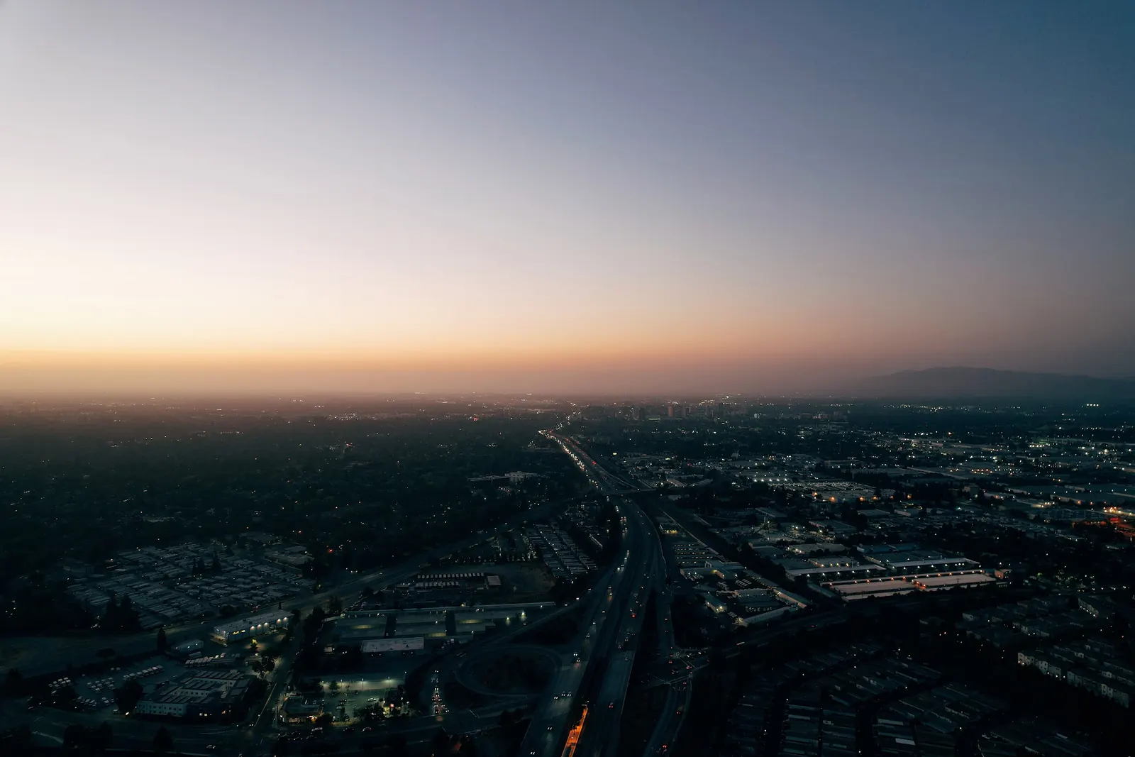 Aerial city at dusk with highway light trails and glowing grid city lights
