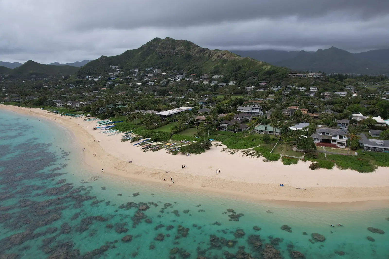 Aerial of tropical beach, outrigger canoes, turquoise reef, and green mountains
